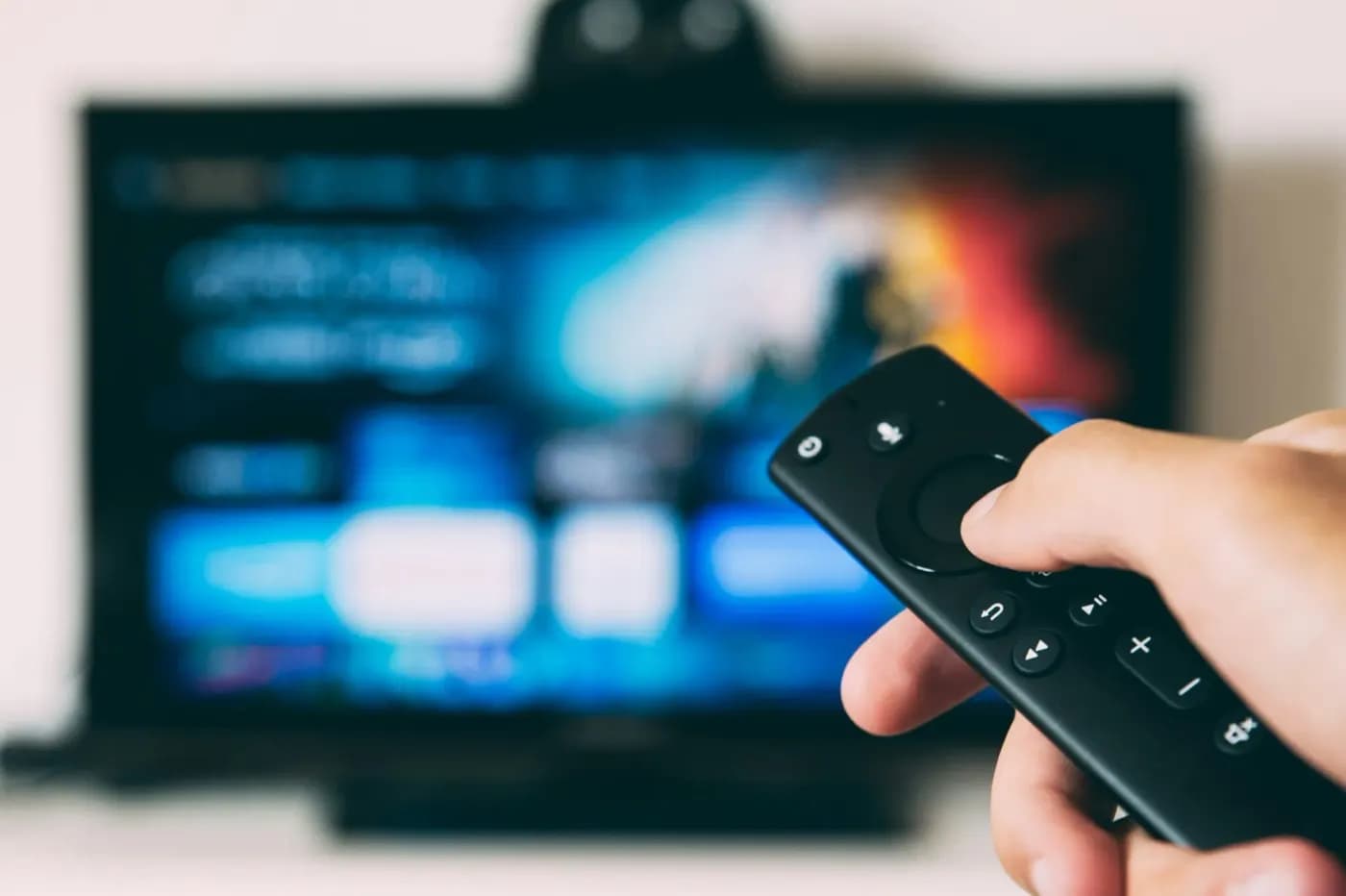 Hand holding a streaming remote in front of a TV app, ready for Zyminex IPTV